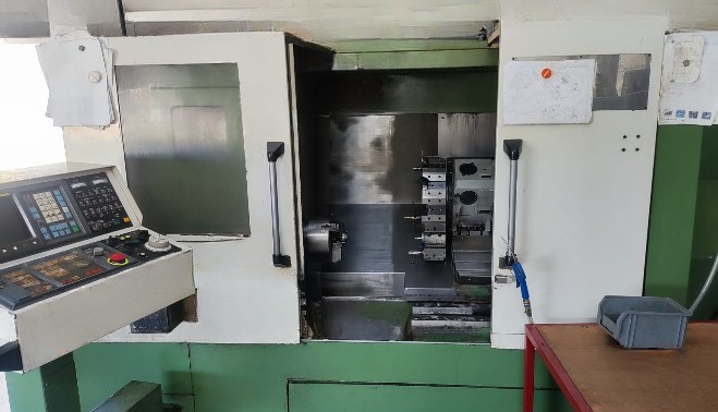 Salle d'usinage avec une machine CNC, commandes sur le panneau latéral.